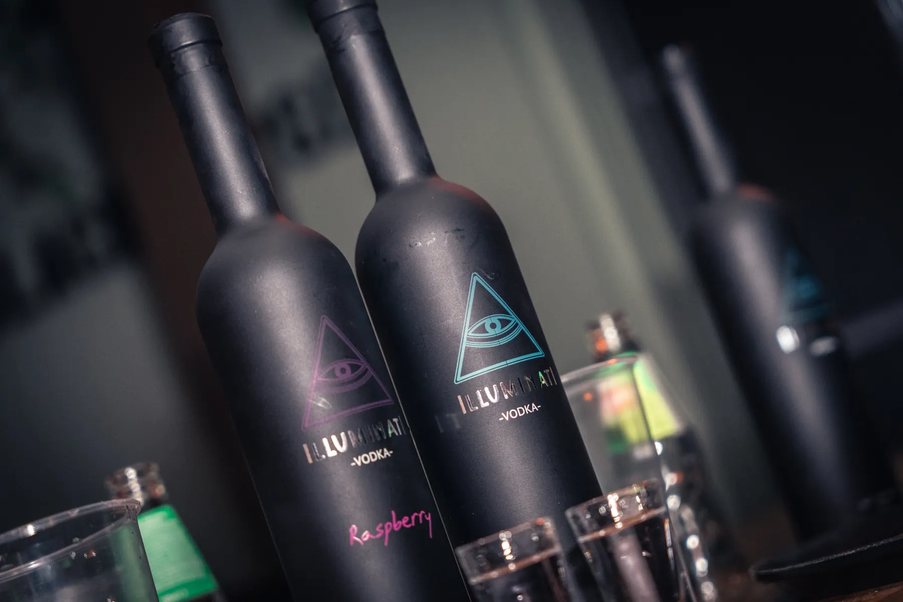 Illuminati Original and Raspberry bottles side by side, their blue and pink eyes lit