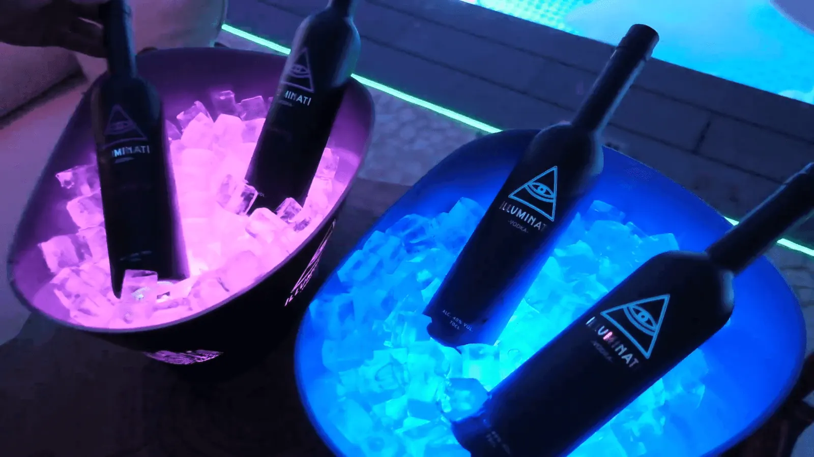 Illuminati Vodka bottles chilling in lit ice buckets beside a pool at night